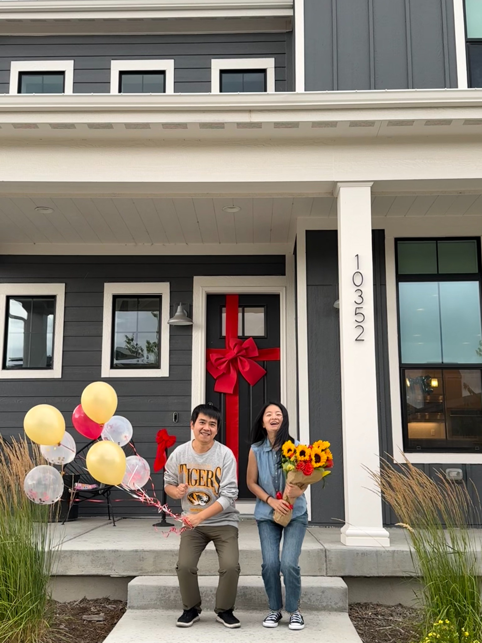 New homeowners celebrating in front of a door decorated with a large red bow