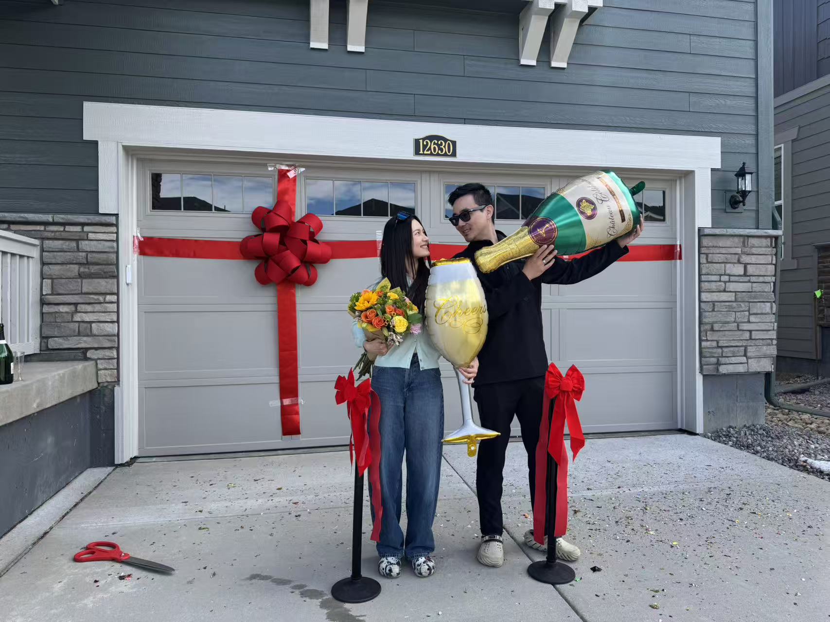 New homeowners celebrating closing in front of a home wrapped with a red gift ribbon